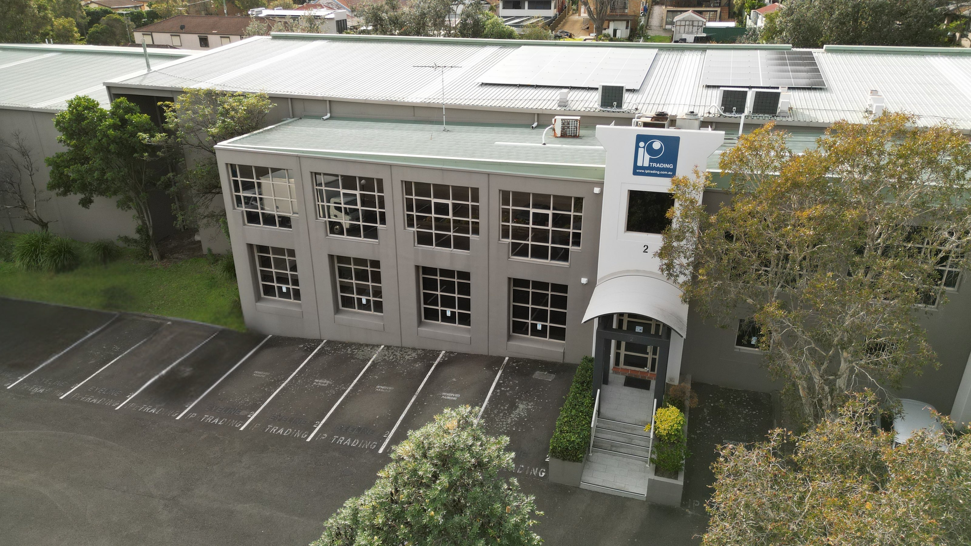 Aerial view of a IP Trading building with a blue sign on the side, surrounded by trees and a parking lot.