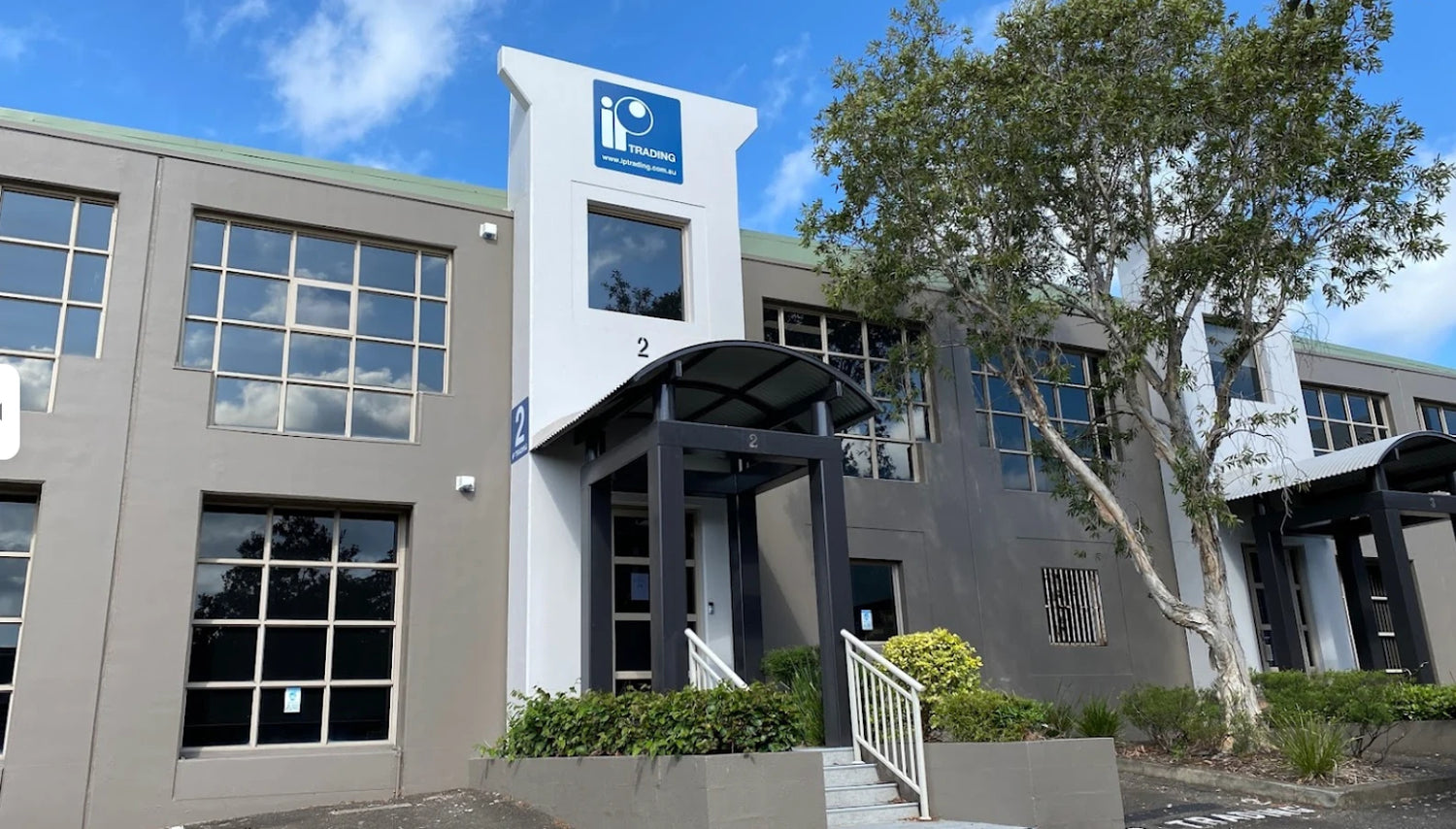 The main object is a modern office building with gray and white exterior walls, large windows, and a prominent blue logo on the central tower.